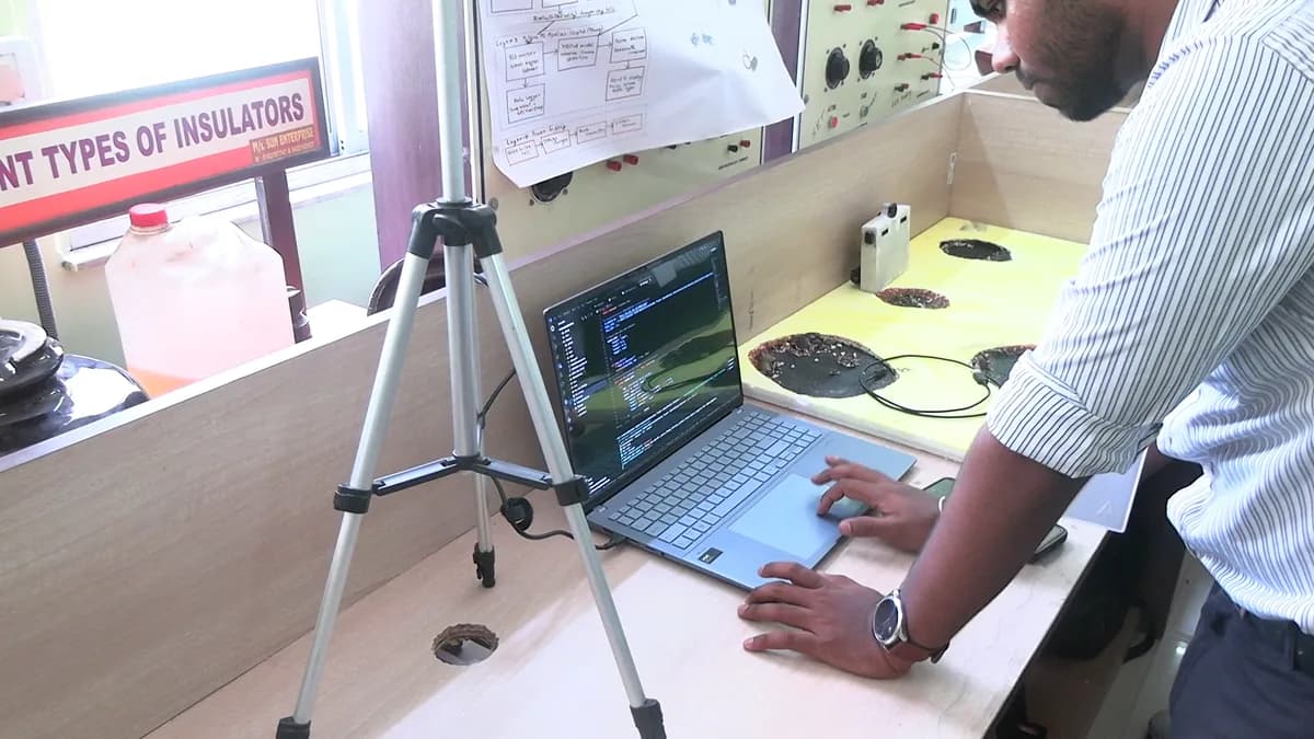 A student demonstrating a laptop-controlled technical setup on a workbench, with an insulator-testing project display in the background, at INNOVENTION 2k26