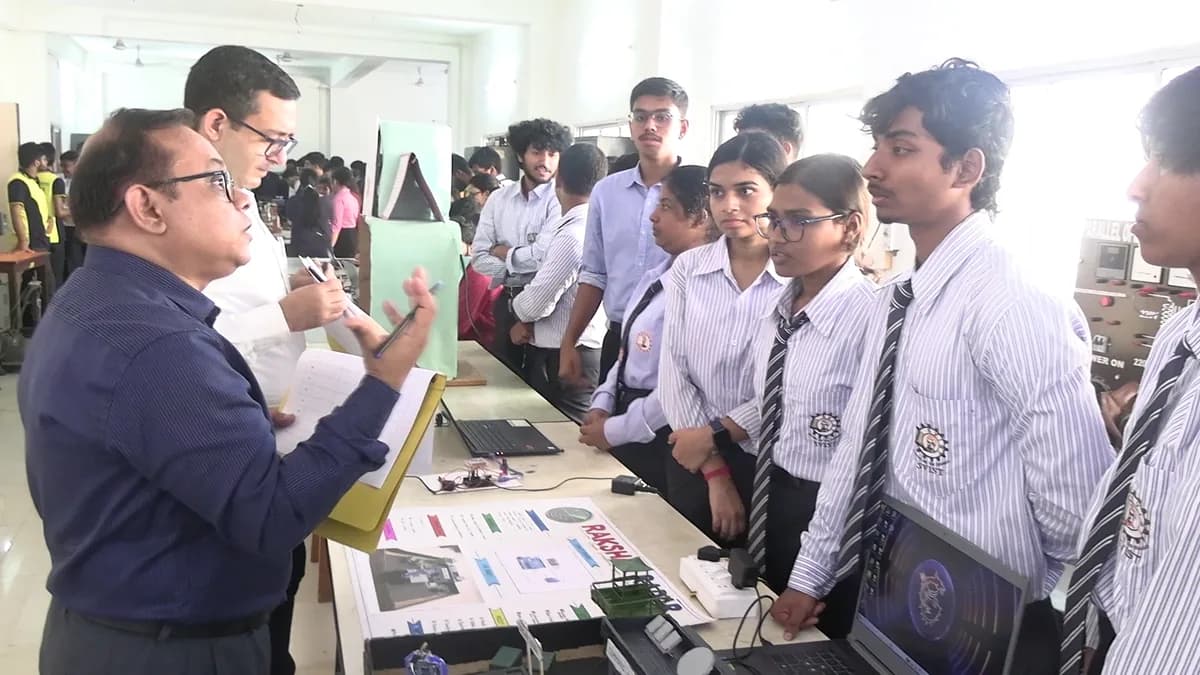 A faculty judge in discussion with a group of students standing behind their project display table, part of the technical exhibition at INNOVENTION 2k26