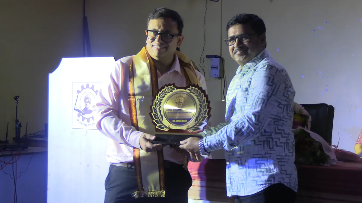 Two men on stage during the inaugural ceremony of INNOVENTION 2k26, one presenting a memento shield to the other in front of the SVIST podium backdrop